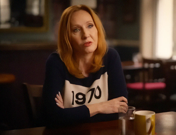 Author J.K. Rowling seated at a table indoors, engaged in conversation related to Harry Potter fans.