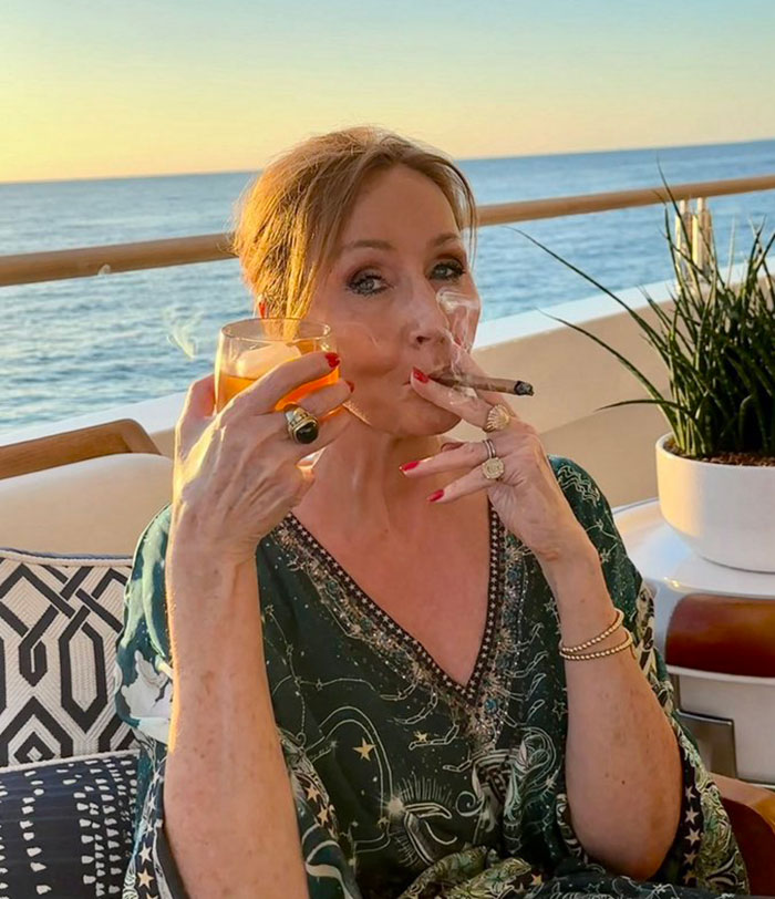 Woman smoking a cigar and holding a drink outdoors with ocean view, related to Pedro Pascal defending criticism of JK Rowling.