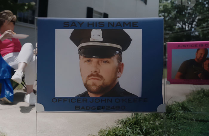 Memorial sign for Officer John O'Keefe with the phrase Say His Name, related to Karen Read trial and slaying controversy.