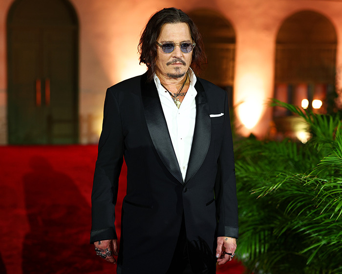 Johnny Depp wearing a black suit and sunglasses at a red carpet event, revealing challenges during Amber Heard trial.