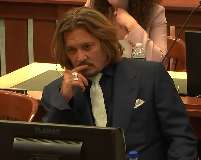 Johnny Depp in courtroom, dressed in suit and tie, appearing thoughtful during Amber Heard trial involving his agent.