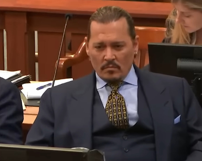 Johnny Depp in courtroom during trial, dressed in suit and tie, with jury and legal staff in background.