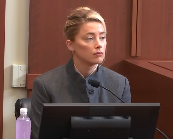 Female juror in courtroom speaking about Johnny Depp trial, seated behind a microphone and computer monitor.