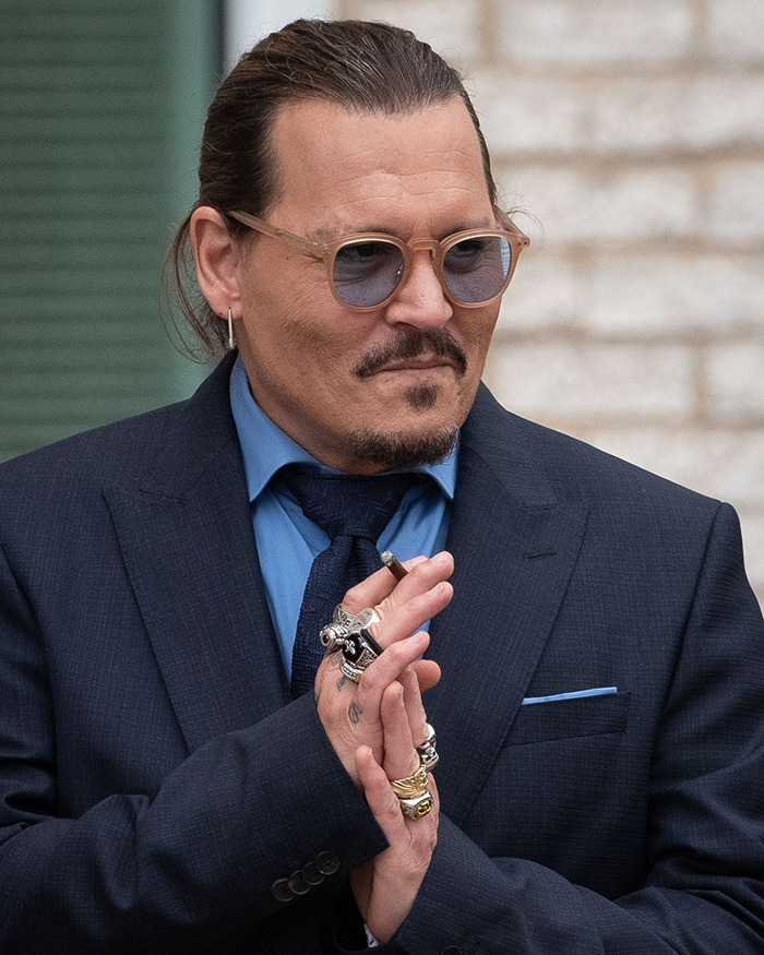 Man in a dark suit and sunglasses with rings and earrings, representing Johnny Depp trial juror courtroom scene.