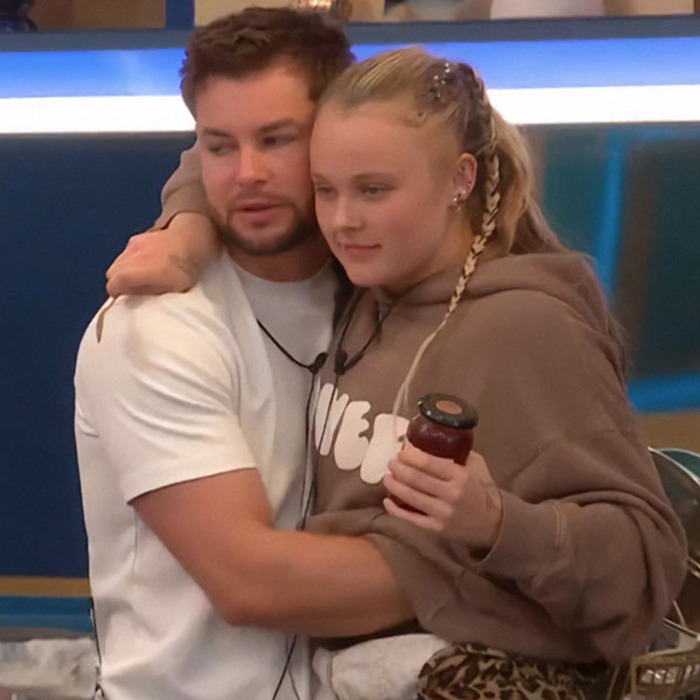 JoJo Siwa hugging a man indoors, wearing a brown hoodie, with a post about orientation sparking Pride Month backlash.