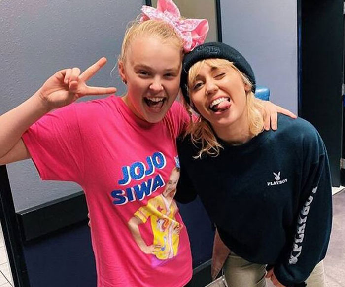 JoJo Siwa posing with Miley Cyrus, both smiling and making playful gestures in a casual indoor setting. JoJo Siwa posing with Miley Cyrus, both smiling and making playful gestures in a casual indoor setting.