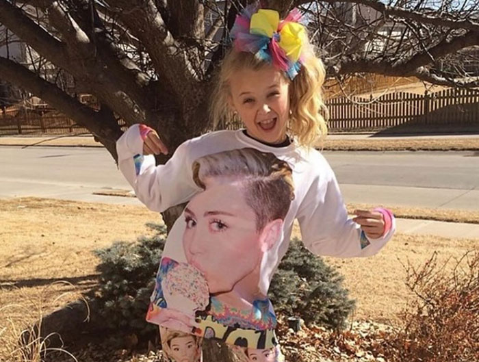JoJo Siwa posing outdoors in colorful outfit after Miley Cyrus' controversial Pride joke backlash, showing confident expression. JoJo Siwa posing outdoors in colorful outfit after Miley Cyrus' controversial Pride joke backlash, showing confident expression.