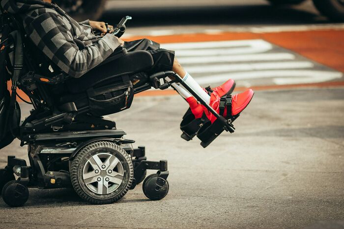 Person in a motorized wheelchair wearing bright red shoes on a city street, reflecting challenges of being big in Japan.