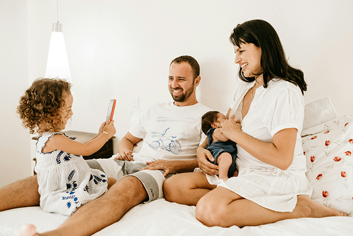 Family with dad and mom sitting on bed smiling while daughter takes photo with smartphone, depicting playground mishap story.