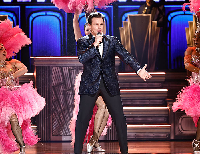 Jonathan Groff performing energetically on stage at the 2025 Tony Awards with dancers in vibrant pink costumes.
