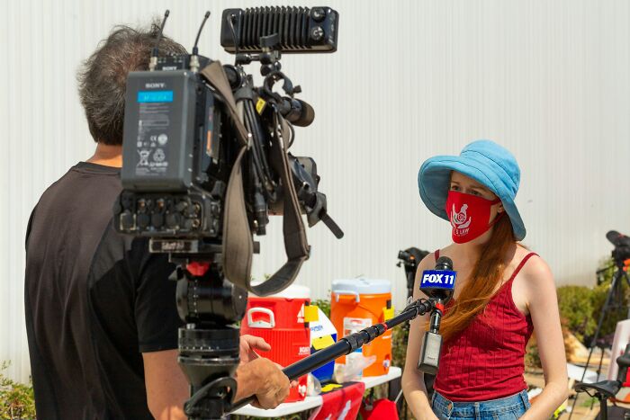 Reporter wearing a red mask and blue hat conducting an outdoor interview about fictional things still believed real.
