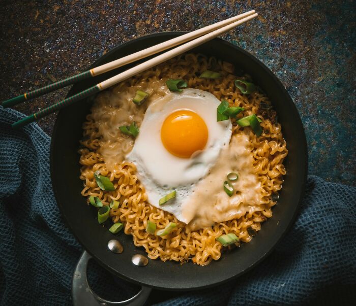 Frying pan with cooked noodles topped with a sunny side up egg and chopped green onions with chopsticks resting on top
