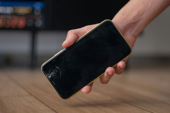 Hand holding a c*****d smartphone screen, illustrating poor people habits that persist regardless of wealth.