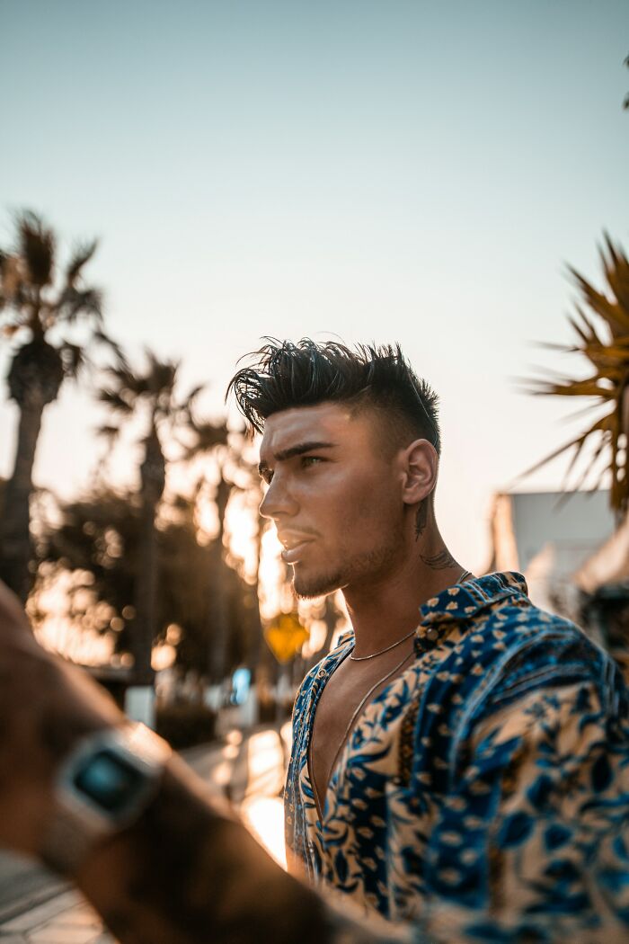 Young man with styled hair in patterned shirt outdoors at sunset, capturing a moment of realizing a close friend is a total jerk.