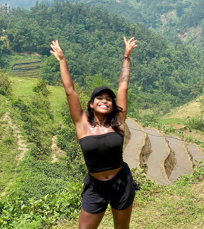 Young woman smiling and raising hands outdoors in lush green area, related to volcano tours and tourism controversies. Young woman smiling and raising hands outdoors in lush green area, related to volcano tours and tourism controversies.