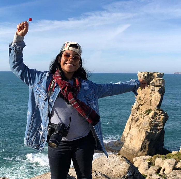 Woman smiling at a coastal cliff, representing the guide accused of abandoning tourist in active volcano incident. Woman smiling at a coastal cliff, representing the guide accused of abandoning tourist in active volcano incident.