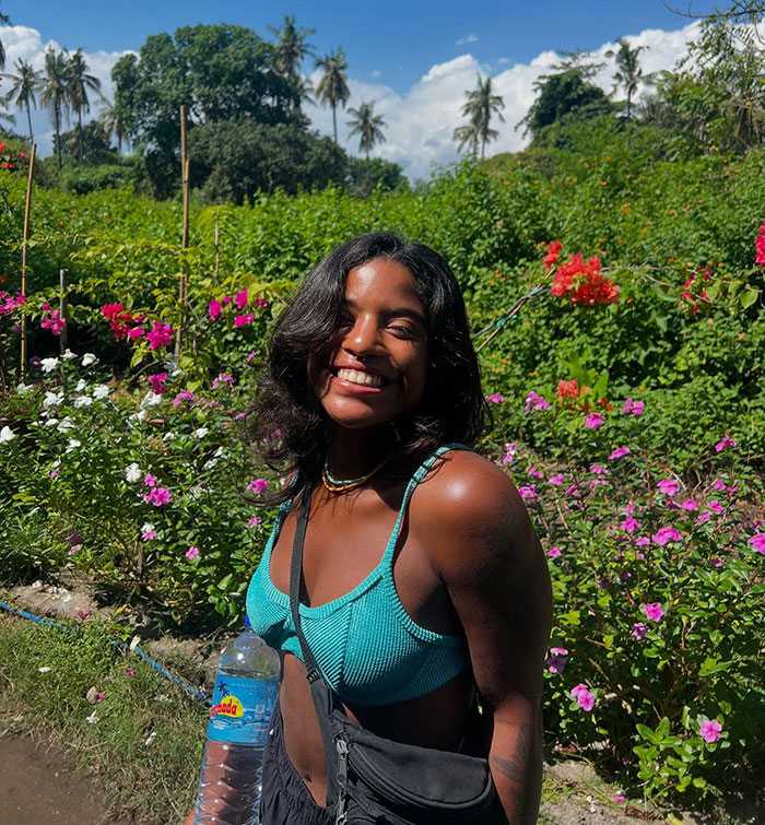 Smiling female tourist in blue top posing in lush garden before hike on Indonesian volcano where she was abandoned and went missing