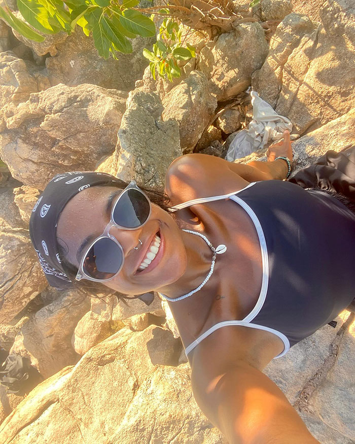 Female tourist wearing sunglasses and bandana, smiling while hiking on rocky terrain near Indonesian volcano.