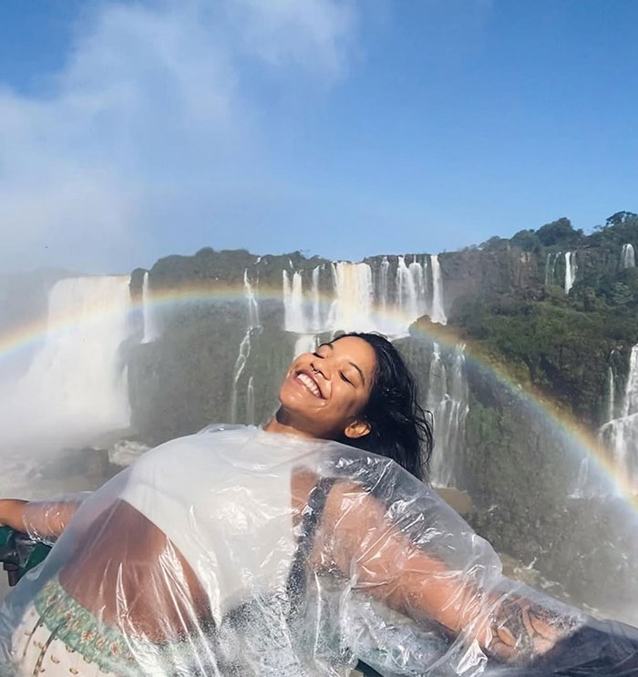 Woman smiling and wearing a rain poncho near waterfall with rainbow, unrelated to guide accused of abandoning tourist in active volcano. Woman smiling and wearing a rain poncho near waterfall with rainbow, unrelated to guide accused of abandoning tourist in active volcano.