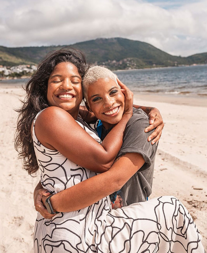 Two women embracing happily on a beach with mountains and water in the background, related to volcano rescue guide news. Two women embracing happily on a beach with mountains and water in the background, related to volcano rescue guide news.