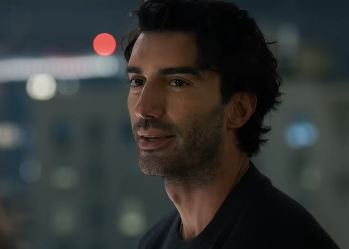 Close-up of a man with dark hair and beard speaking thoughtfully against a blurred city night background.