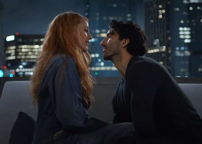 Couple sitting close on rooftop at night in city with blurred lights, evoking emotion and connection between two people.