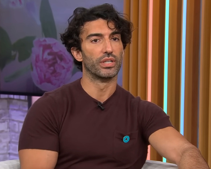 Man with curly hair in brown shirt speaking during a televised interview about Justin Baldoni's lawyer responding to lawsuit dismissal.