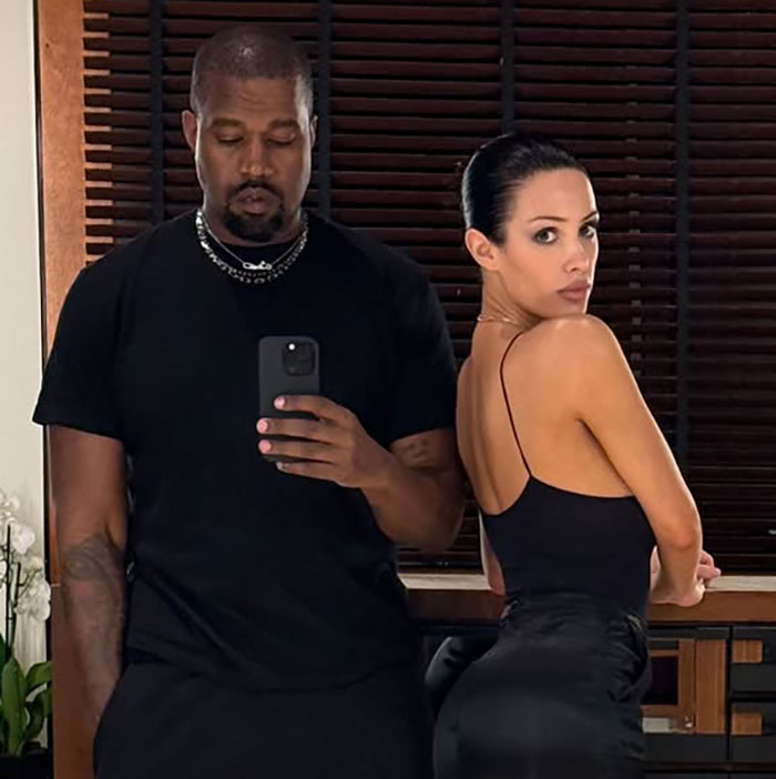 Kanye West and his wife Bianca Censori posing indoors, highlighting Bianca in a black outfit and sleek hairstyle.