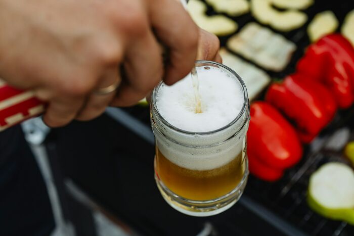 Pouring beer into a glass at a barbecue with vegetables grilling, highlighting big no no cultural etiquette.
