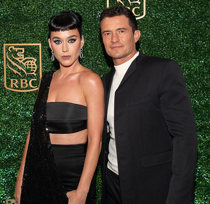 Katy Perry and Orlando Bloom posing together at an event, dressed in black with a green hedge background. Katy Perry and Orlando Bloom posing together at an event, dressed in black with a green hedge background.