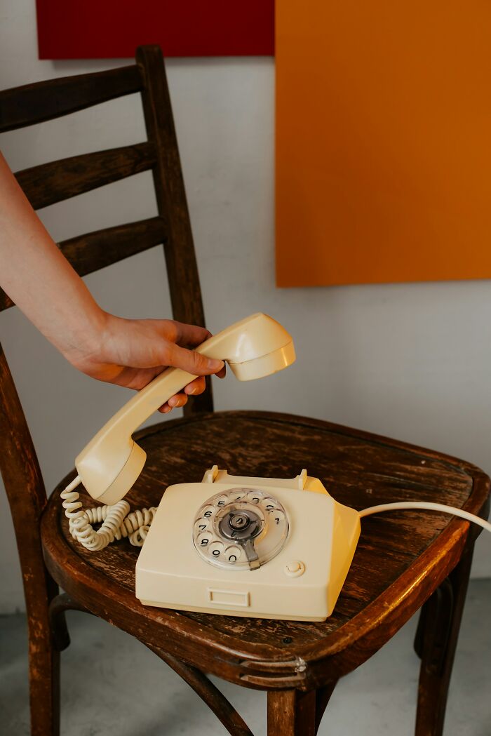 Hand holding receiver of rotary phone on wooden chair, symbolizing childhood joys before smartphones and life not recorded.