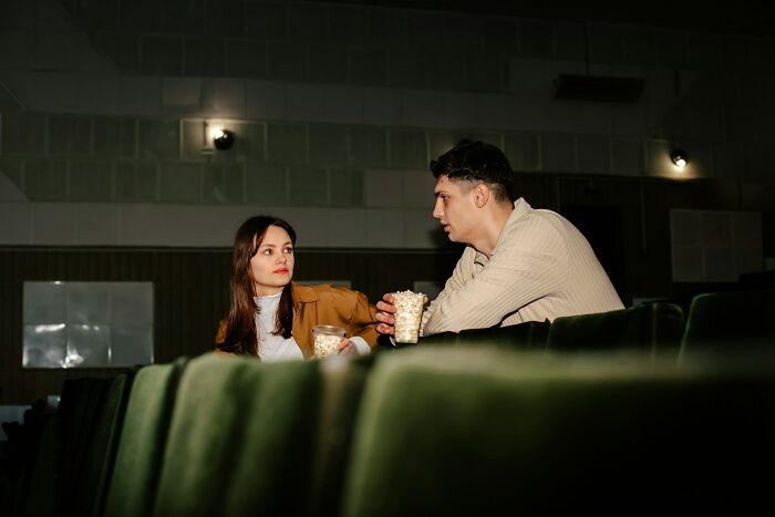 Two friends in a dimly lit room sharing popcorn, capturing a moment of realization about a close friend being a total jerk.