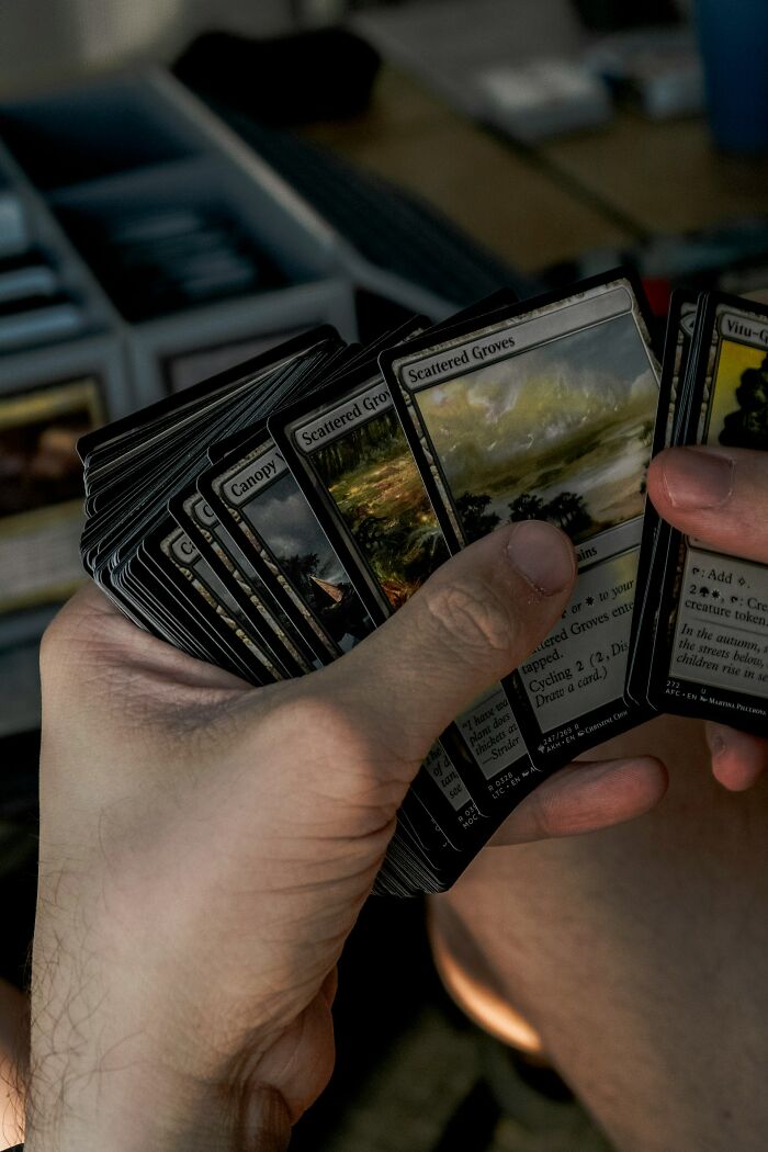 Person holding and fanning collectible cards, focusing on scattered groves cards in a casual gaming moment.