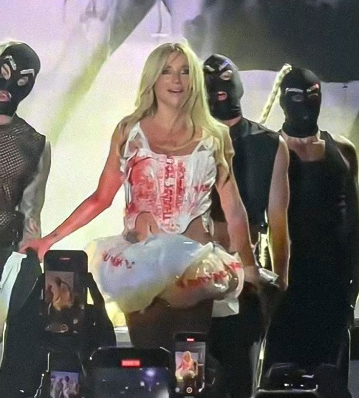 Kesha performing at Mighty Hoopla with dancers in masks, engaging in a controversial and provocative act on stage.