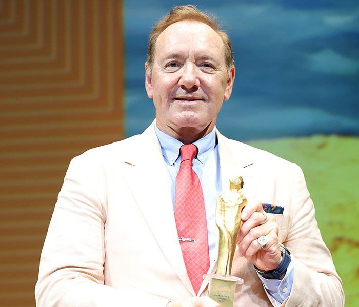 Kevin Spacey holding an award on stage, sparking plastic surgery rumors after his recent red carpet appearance.