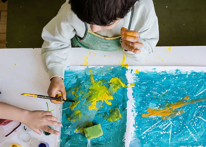 Child painting with yellow and blue colors, illustrating creativity while MIL shocked her son over wife's pregnancy.