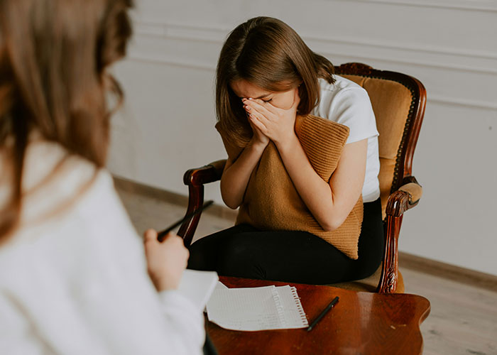 Woman covering her face in distress while sitting during a tense conversation about MIL shocked her son kicking her out.