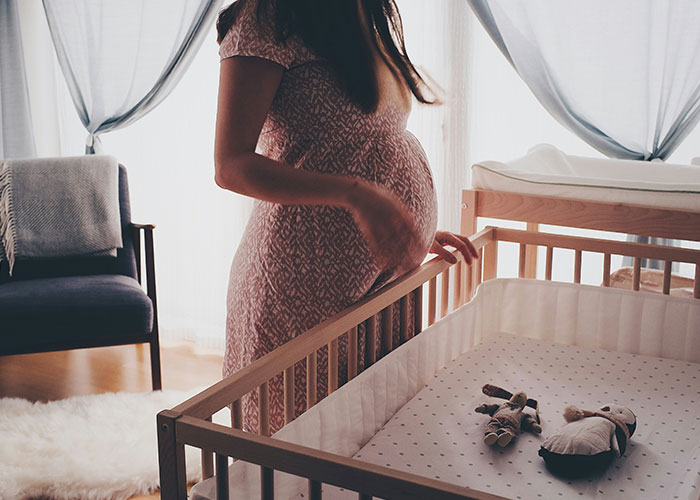 Pregnant woman standing by a crib in a nursery, symbolizing a family conflict over wife's pregnancy and MIL.