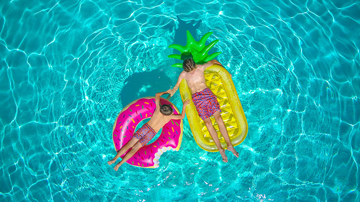 Two kids floating on colorful pool floats in clear blue water, enjoying a birthday celebration outdoors.