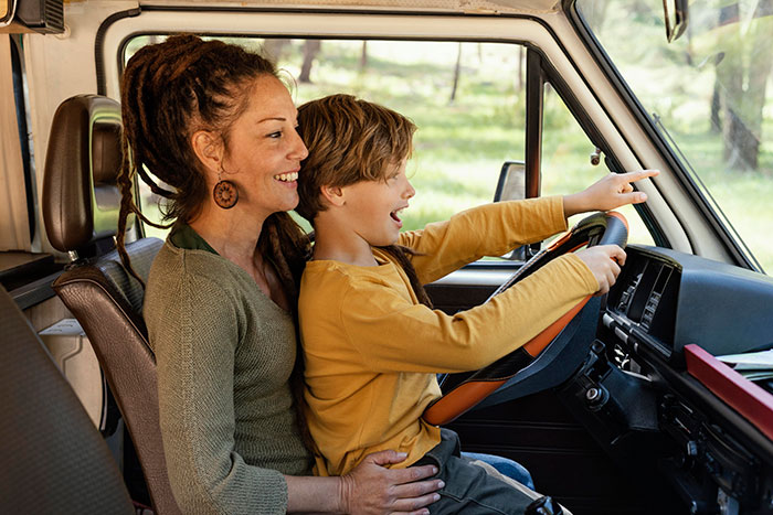 Mom and kid celebrating birthday with joyful expressions, kid pointing ahead while sitting on mom's lap inside a vehicle.
