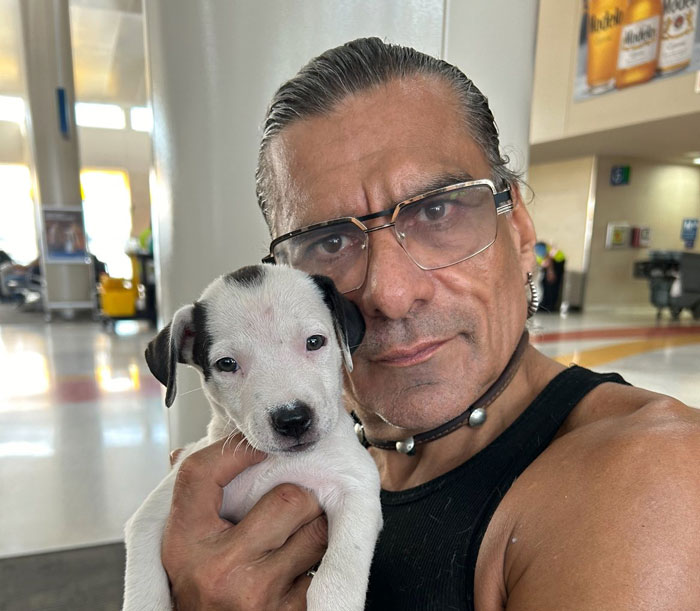 Man holding small white and black puppy indoors, related to King Of The Hill voice actor Jonathan Joss news.