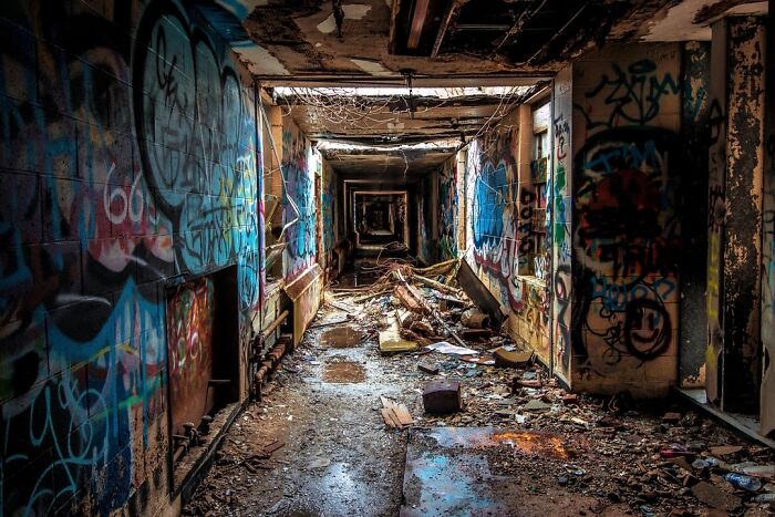 Abandoned explorers' creepy encounter in a graffiti-covered, debris-strewn hallway of a decaying, forgotten building.