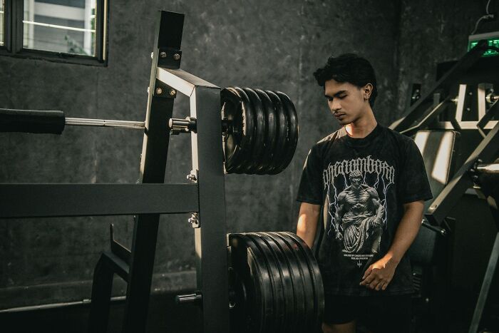 Young man at gym preparing heavy weight plates on a squat rack, illustrating strength and fitness training concepts.