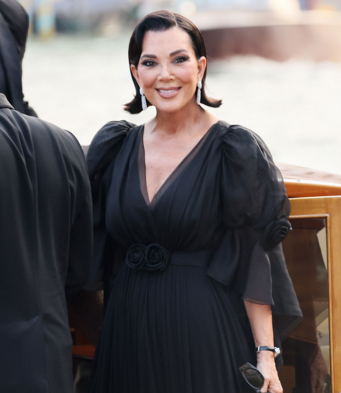 Woman in elegant black dress with puffed sleeves and statement earrings at celebrity wedding welcome party in Venice.