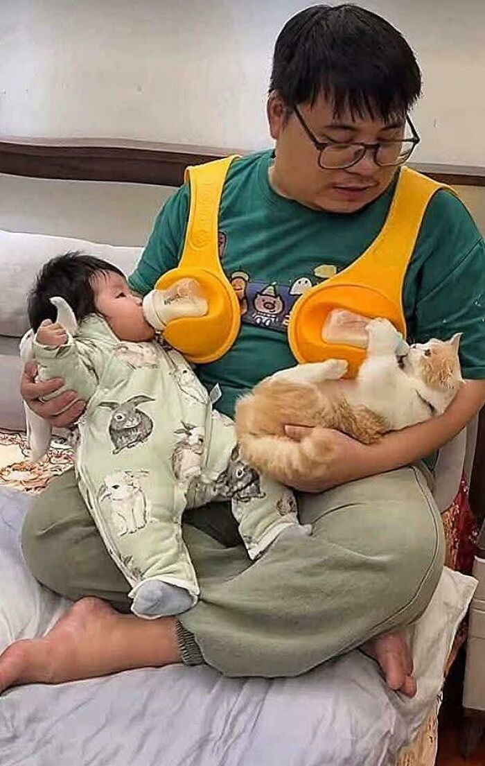 Man feeding a baby and a cat simultaneously with an innovative baby bottle holder in a cozy home setting.
