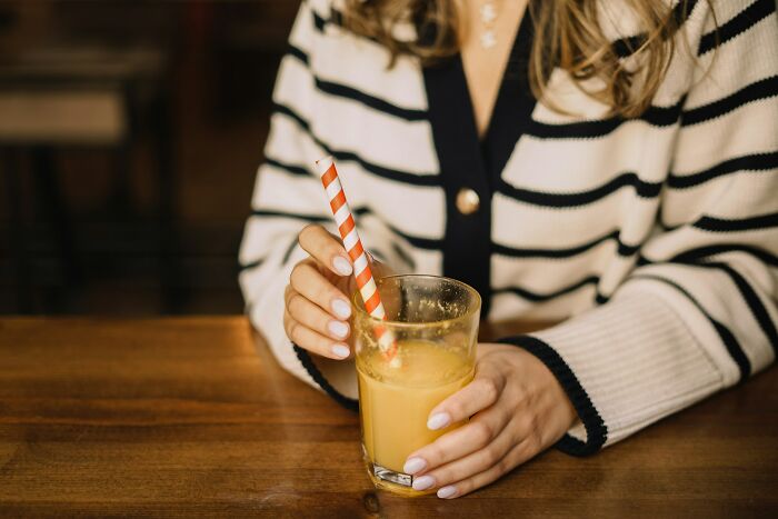 Woman in striped sweater holding glass of juice with striped straw, illustrating pregnancy and twins discussion.