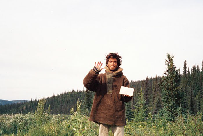 Man in a brown coat waving and holding a note in a forest, one of the last known photos of famous people.