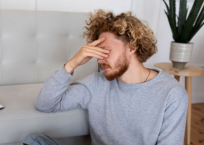 Young man with curly hair covering his face in frustration, illustrating awkward moments during dates with stupid remarks.