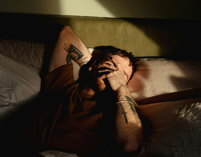 Man with tattoos lying in bed covering his face, representing stressed people lawyers immediately knew are not winning case.