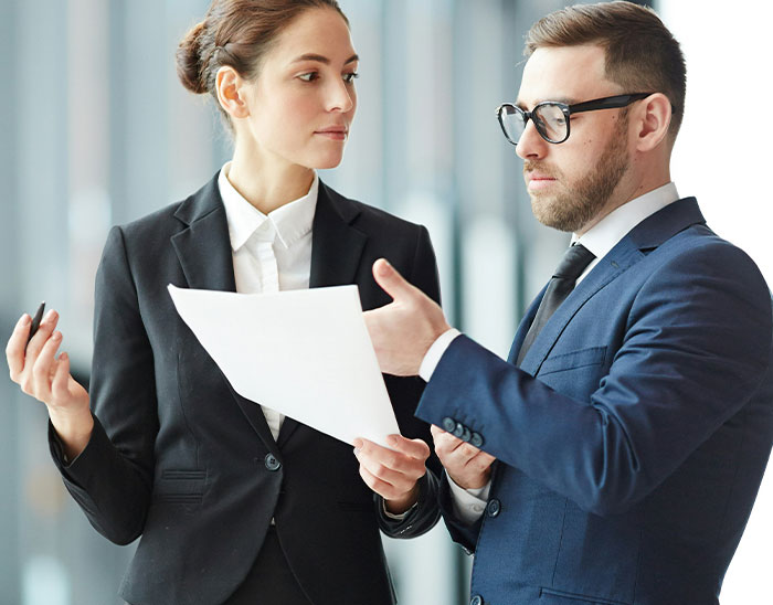 Two lawyers engaged in a serious discussion, reviewing documents and analyzing a case inside a modern office.